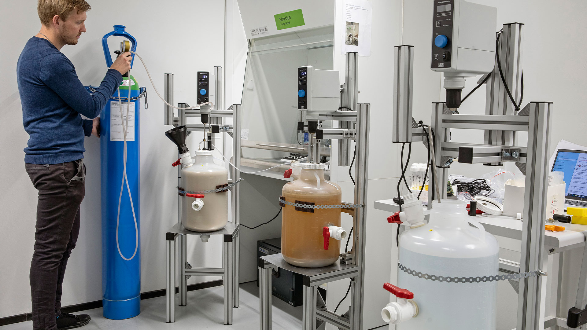 Man adjusting equipment in a lab where several reactors are placed. Photo: Sine Fiig